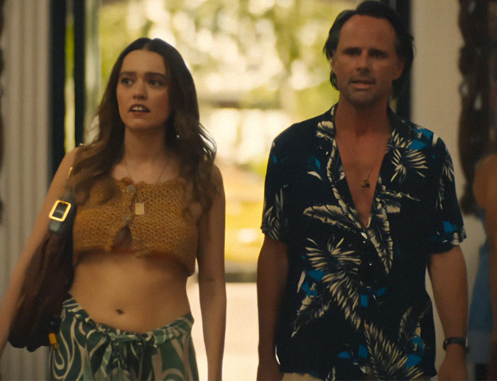 A woman in a crochet top and a man in a floral shirt walking inside, representing a scene from &lsquo;The White Lotus&rsquo;.