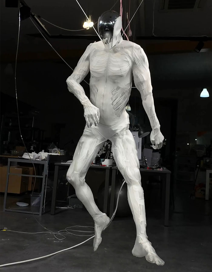 Humanoid robot with lifelike muscles suspended in a workshop environment, showcasing advanced robotics technology.