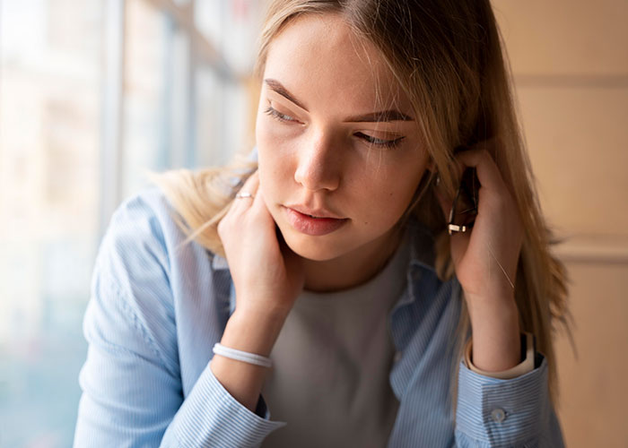 A woman looking thoughtful by a window, contemplating food-related roommate issues.