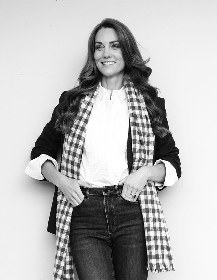 Woman in a checked scarf and black blazer, smiling against a plain background.