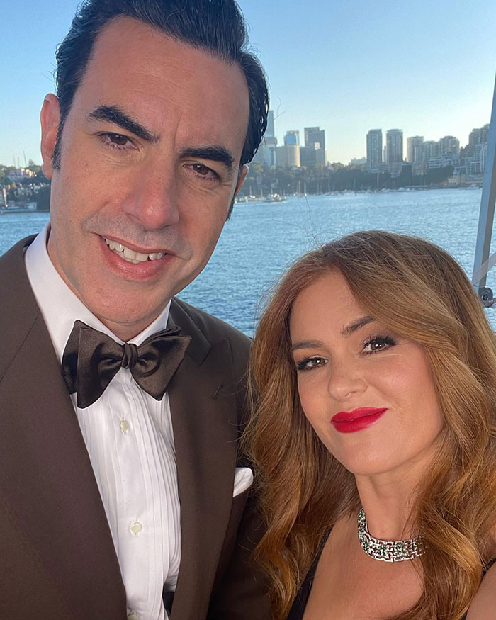 A couple at an event by the water, dressed in formal attire, smiling at the camera.