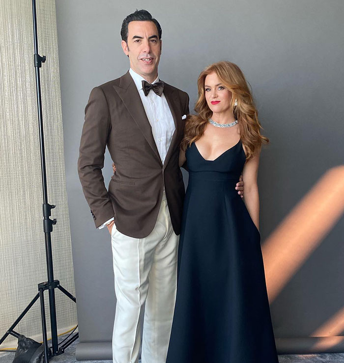 A couple posing elegantly in formal attire against a gray background, connected to Sacha Baron Cohen and divorce news.