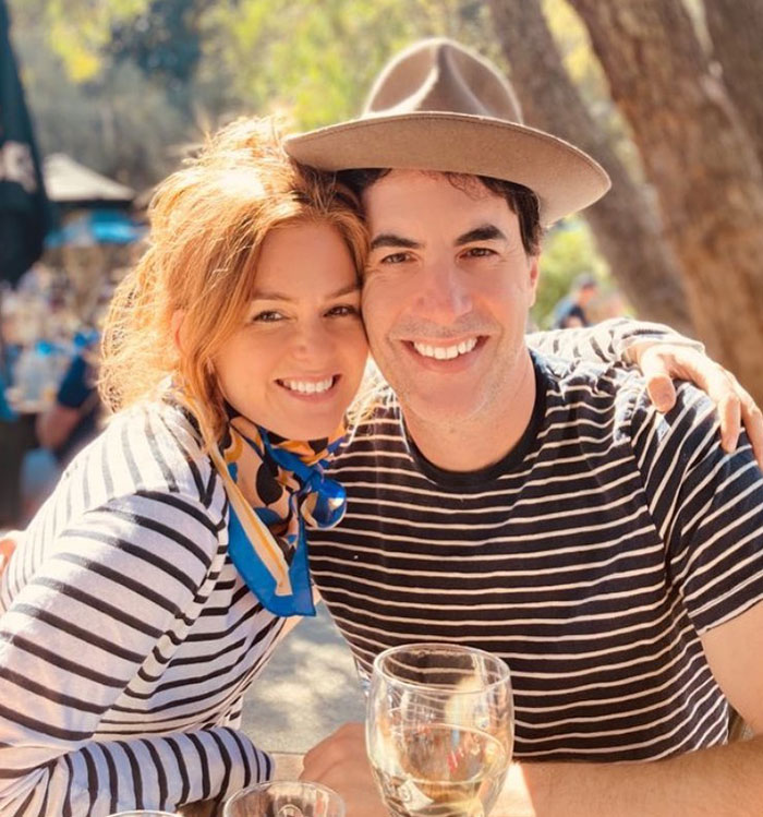 Couple smiling outdoors in striped tops, enjoying a sunny day with glasses of wine, hinting at a past relationship.