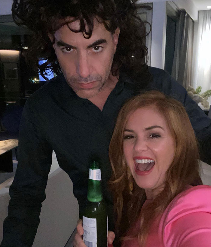 Man and woman smiling in a casual setting, holding a drink; keywords: Sacha Baron Cohen, Isla Fisher, divorce.