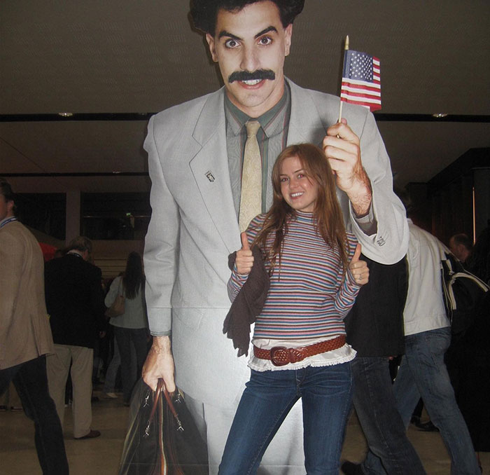 Woman posing with Sacha Baron Cohen cardboard cutout, casually dressed, smiling, indoors.