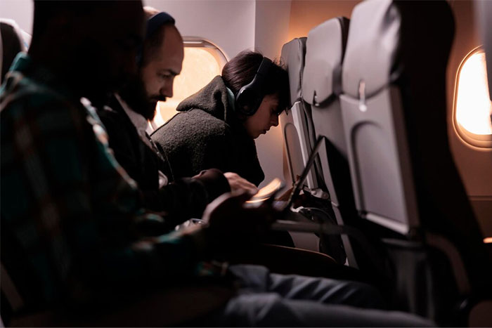 Passengers seated on an airplane, with headphones, viewed from the aisle.