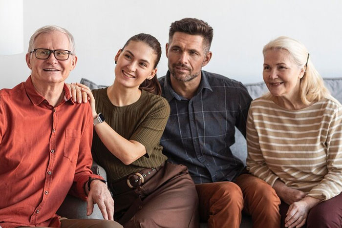 A group of four people sitting on a couch, smiling, with two men and two women in casual attire.