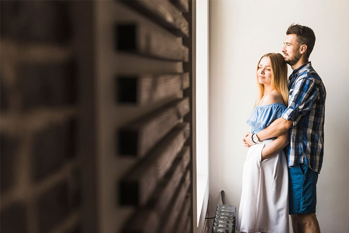 Couple standing by a window, the partner holding the other gently.