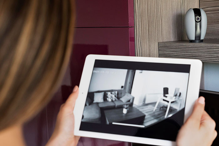 A woman views a home security video on a tablet, showing a living room, emphasizing home intrusion and surveillance.