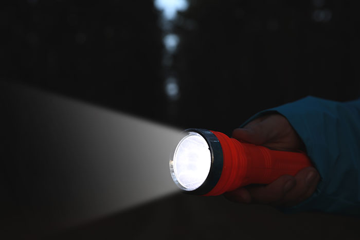 Person holding a red flashlight in the dark, symbolizing breaking into a friend's house.