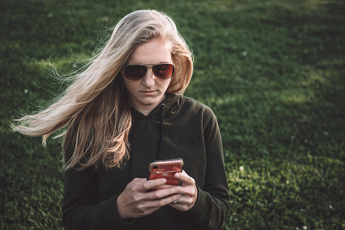 Woman in sunglasses looking at her phone, standing on grass, related to ungrateful sibling situation.