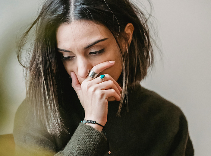 Woman looking concerned, wearing rings and a dark sweater, contemplating after a dispute over "deadbeat mom" remark.