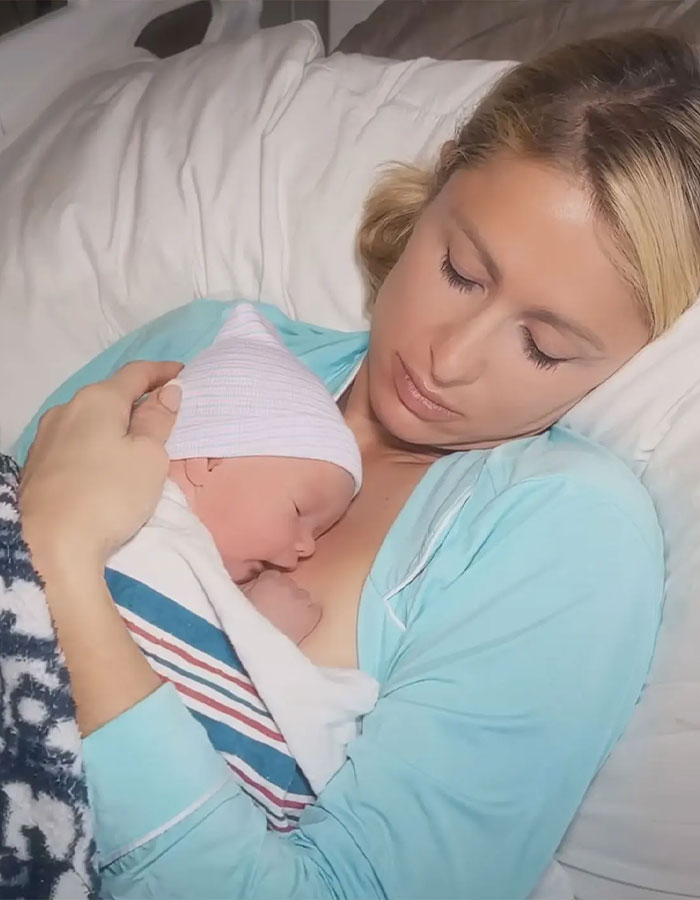 Woman in a hospital bed holding a newborn baby, related to backlash faced by celebrities with surrogate babies.