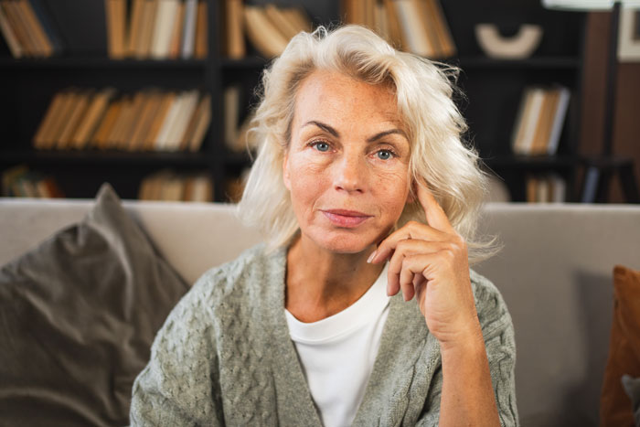 Woman in a living room setting, wearing a gray cardigan, contemplating family dynamics.