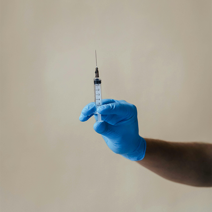 Gloved hand holding a syringe, highlighting Covid vaccines.