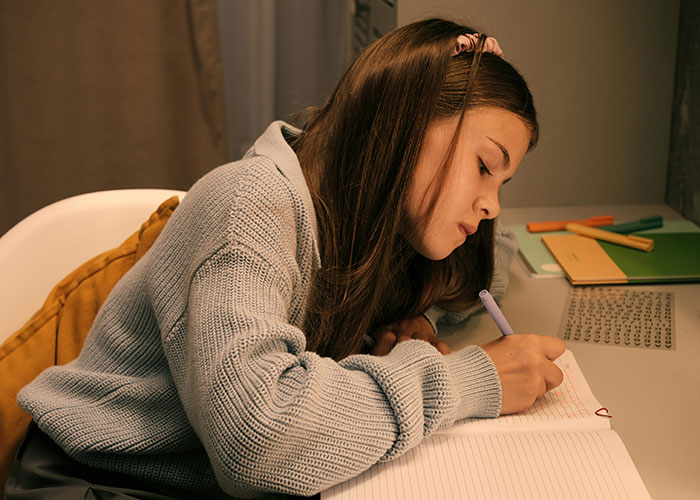 Girl in a blue sweater writing in a notebook, possibly reflecting on a strange punishment experience.