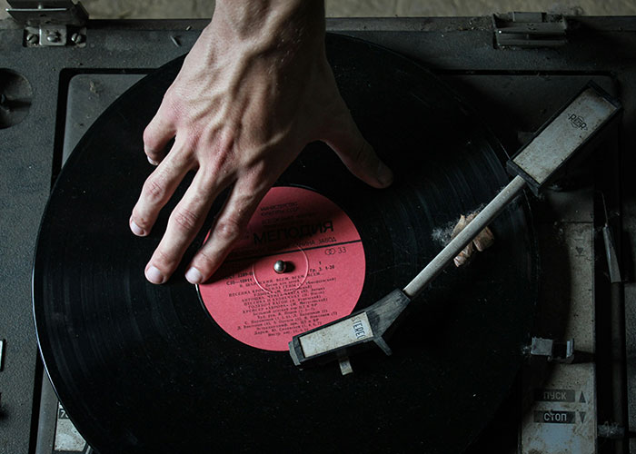 Hand on a vinyl record player, illustrating a strange punishment concept.