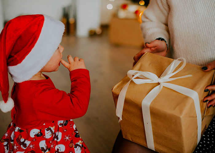 Child in a Santa hat receiving a wrapped present from a parent, holding it as part of an unusual punishment narrative.