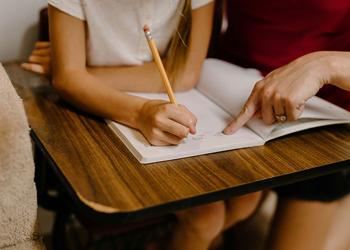 Child writing in notebook as adult points, illustrating a unique parental punishment concept.