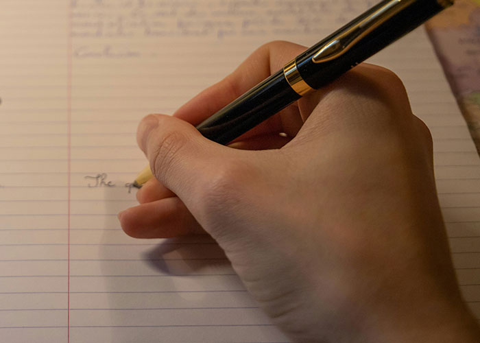 Person writing on lined paper with a black pen, illustrating punishment concepts.