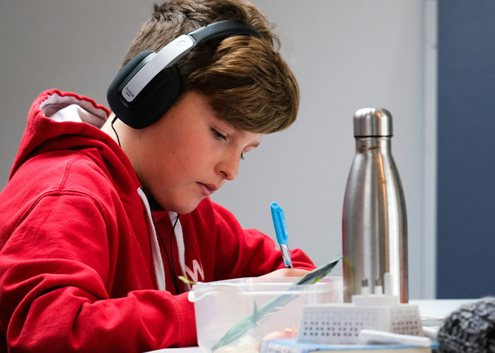 Child wearing headphones and a red hoodie, writing at a table with focus, related to strange punishment stories.