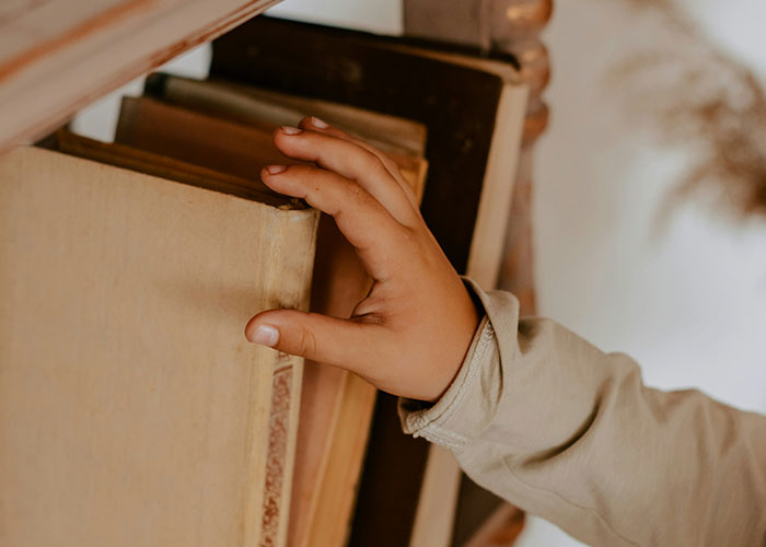 Child's hand reaching for a book on a shelf, related to unusual punishments from parents.