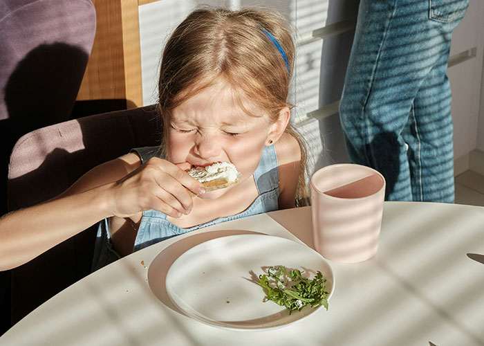 Child eating food with an upset expression, possibly experiencing strange punishment.