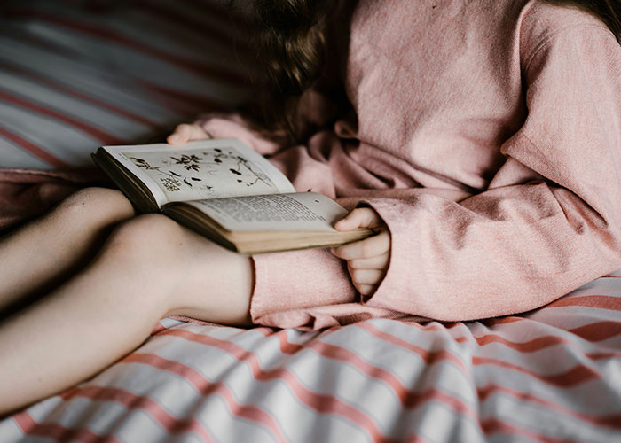 Child in pink dress reading a book on a bed, related to strangest punishment discussion.