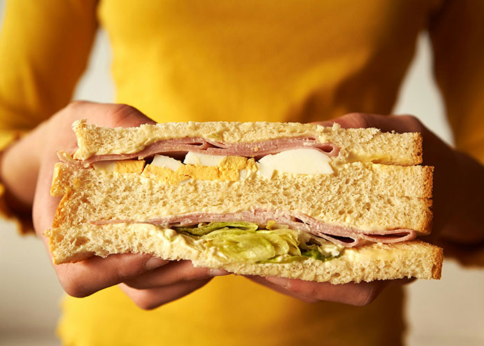 Person holding a large sandwich with multiple layers of fillings, illustrating a unique punishment story from parents.