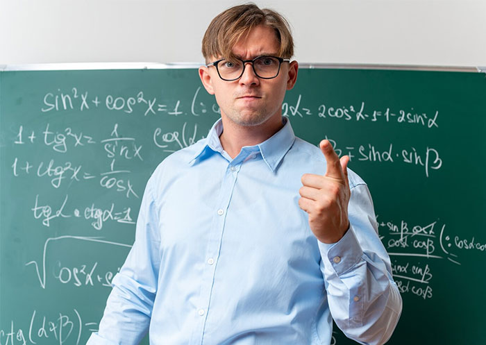 Teacher in front of a chalkboard with math equations, wearing glasses and a blue shirt.