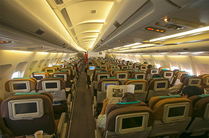 Airplane cabin interior showcasing closely arranged seats, typical of corporate propaganda normalization.