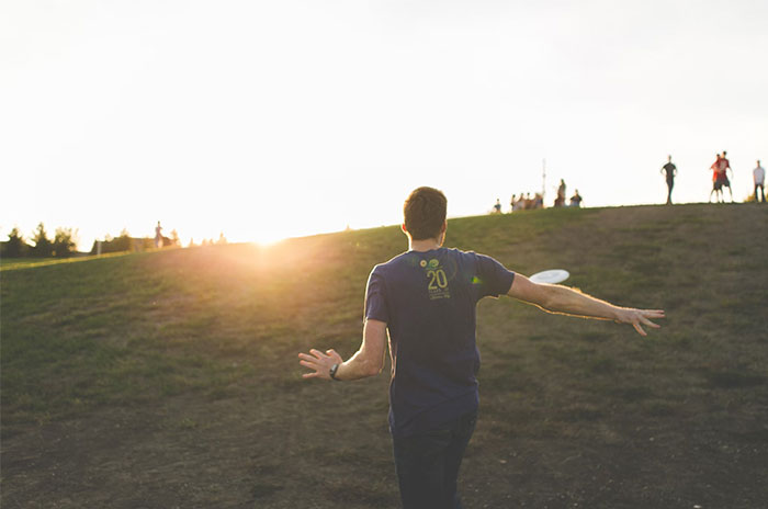 Person playing frisbee on a hill at sunset, illustrating normalized activities influenced by corporate propaganda.