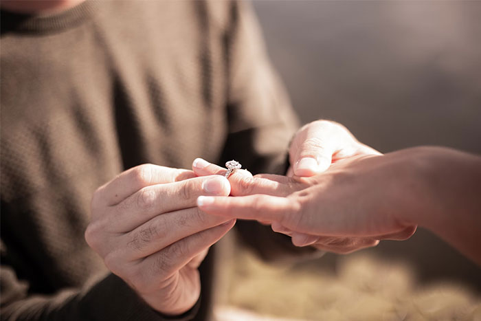 Placing a ring on a finger, symbolizing engagement or commitment, often influenced by corporate propaganda.