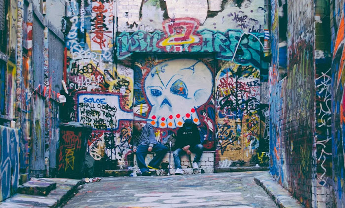 Two people sitting in a graffiti-covered alley, highlighting impacts of corporate propaganda normalization.