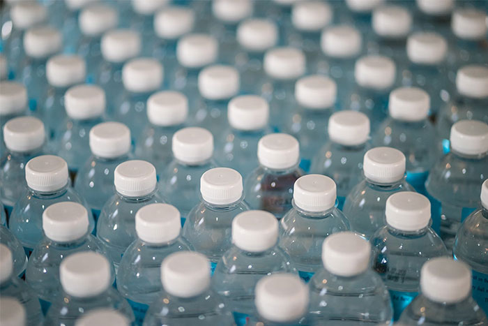 Rows of plastic water bottles with white caps, illustrating corporate propaganda normalization.