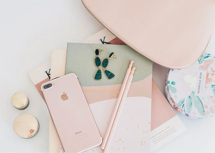 Stylish desk layout featuring a smartphone, gold earrings, and pink stationery, highlighting corporate propaganda aesthetics.