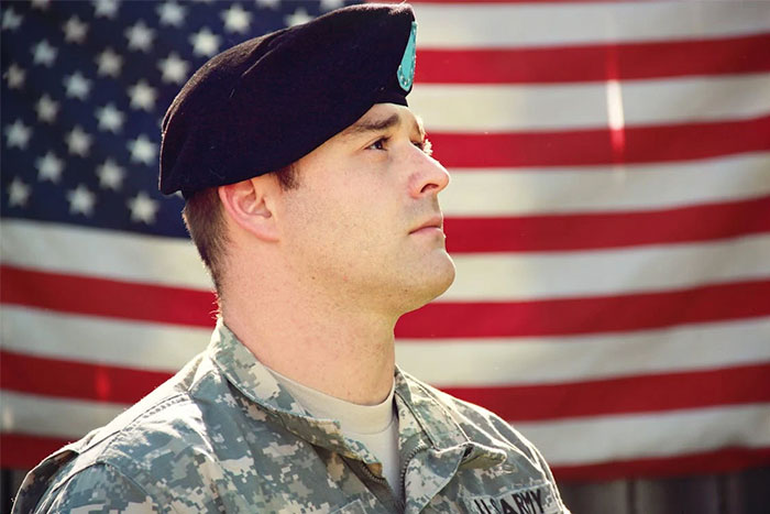 Soldier in uniform with US flag backdrop, illustrating themes of corporate propaganda.