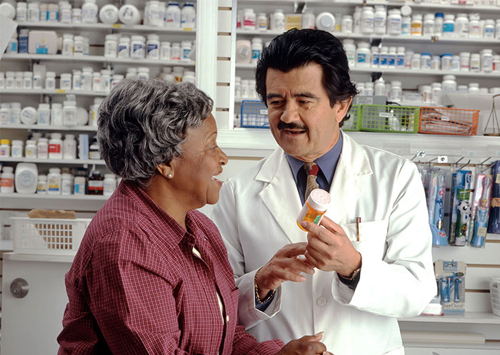 Pharmacist showing medication to a customer, highlighting normalized practices through corporate propaganda.