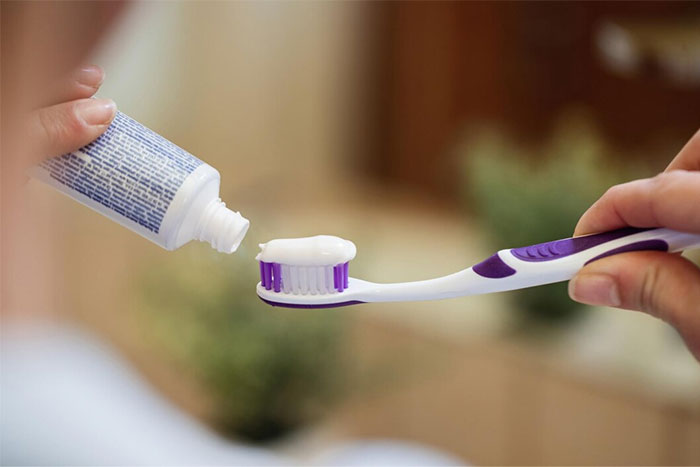 Toothpaste being applied on a toothbrush, concept linked to corporate propaganda norms.