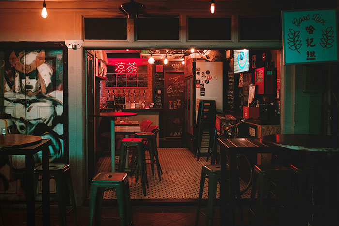 Interior of a dimly lit restaurant with empty tables and stools, featuring a red neon sign, indicating a bad restaurant.