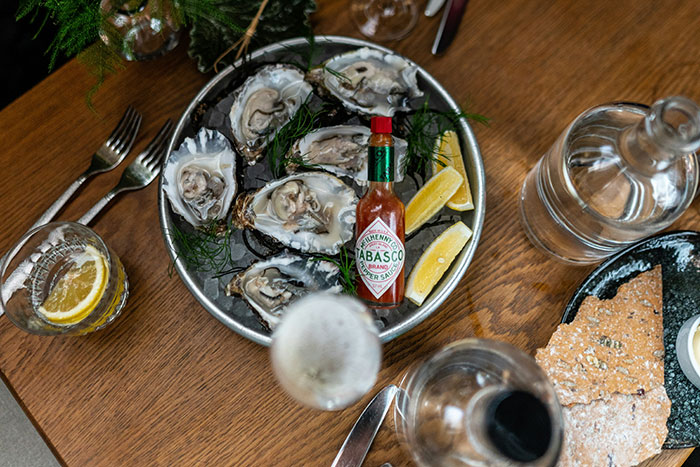 Plate of oysters with lemon and Tabasco sauce, surrounded by glasses and bread, suggesting a potentially bad restaurant experience.