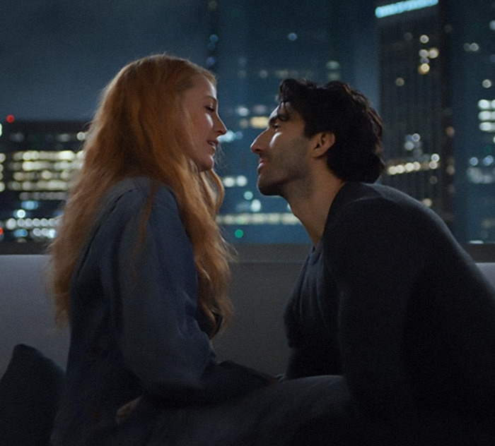 Two people sitting closely on a rooftop at night with a city skyline in the background.