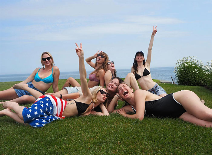 Group of friends smiling and posing on grass by the sea, highlighting pop star lifestyle.