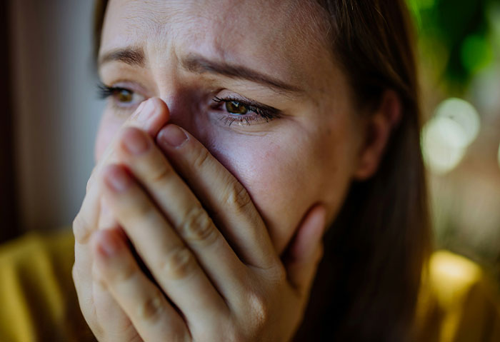 A woman looks anxious, covering her mouth with her hands, concerned about a student's comment.