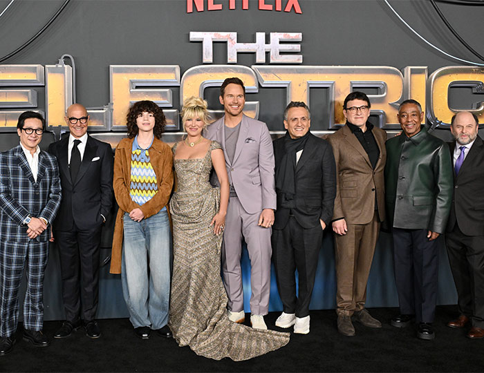 Cast of The Electric State at film premiere, posing together in front of the movie logo.