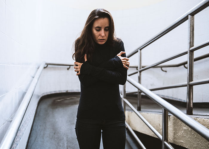 Woman in a dimly lit stairwell, wearing a dark outfit, arms crossed, contemplating relationships and understanding women.