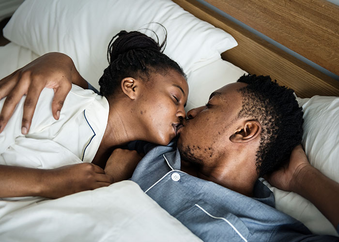 Couple kissing and embracing in bed, highlighting relationship dynamics between men and women.