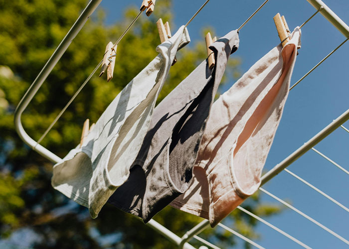 Three pairs of women's underwear drying on a clothesline under a clear blue sky.