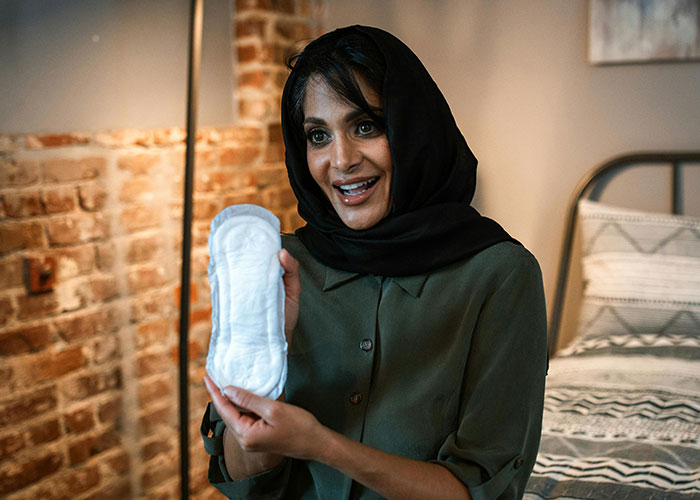 Woman smiling, wearing a headscarf, and holding a sanitary pad, illustrating surprising lessons men learn about women.