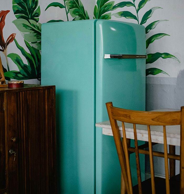 Vintage green fridge in a kitchen with leafy wallpaper, illustrating frugality in retro style.